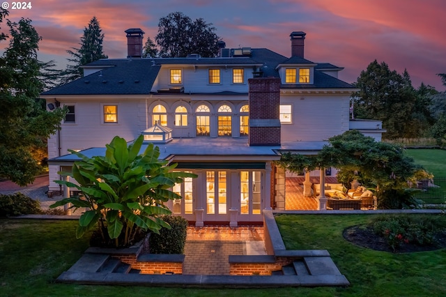 back house at dusk with a lawn, a patio area, and french doors