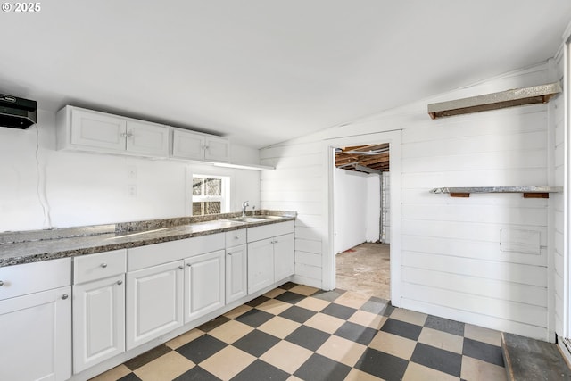 kitchen with vaulted ceiling, white cabinetry, wood walls, and sink