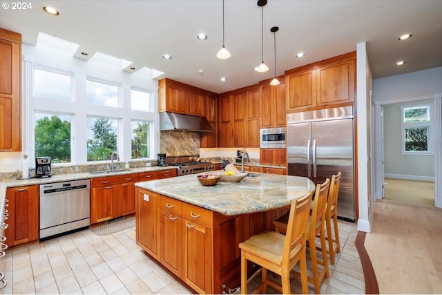 kitchen featuring sink, built in appliances, pendant lighting, a kitchen island, and exhaust hood