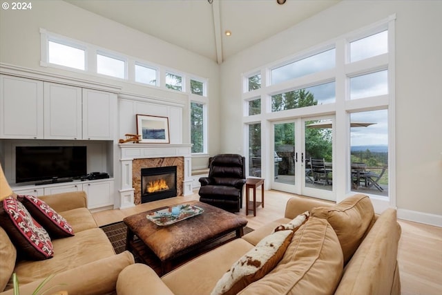 living room with light hardwood / wood-style floors, a towering ceiling, a high end fireplace, and french doors