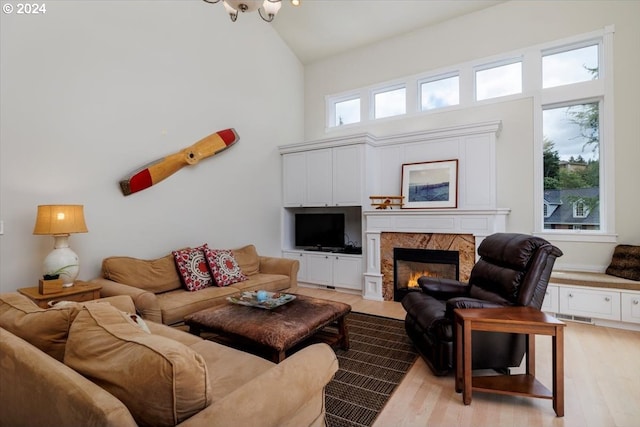 living room with a wealth of natural light, a high end fireplace, light hardwood / wood-style floors, and high vaulted ceiling