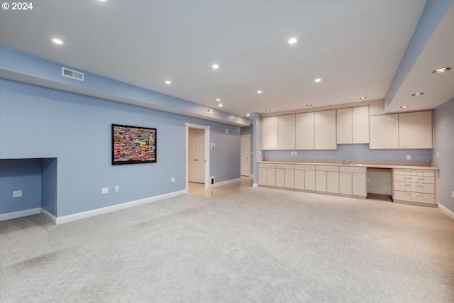 unfurnished living room featuring light colored carpet and built in desk