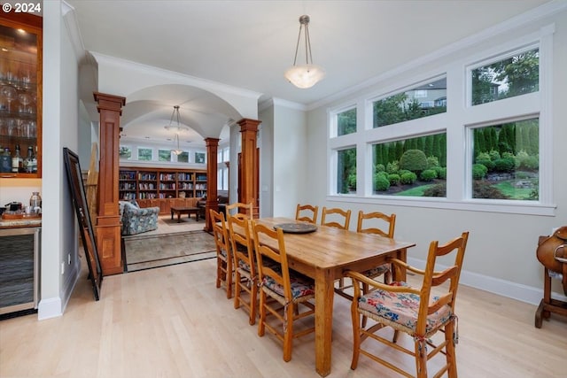 dining space with ornate columns, a wealth of natural light, beverage cooler, and ornamental molding