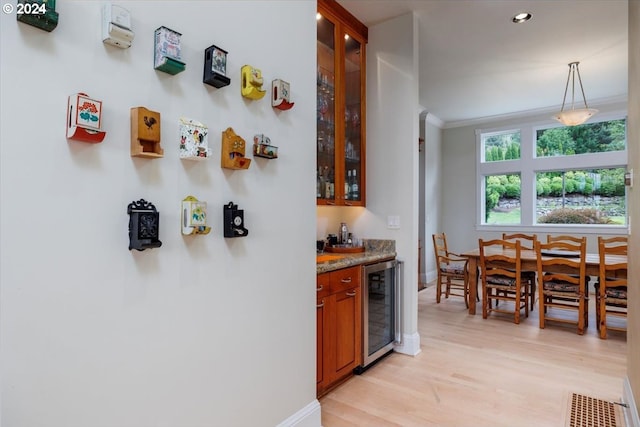 kitchen featuring light stone counters, beverage cooler, crown molding, light hardwood / wood-style flooring, and hanging light fixtures