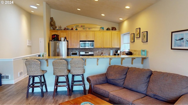 kitchen featuring light brown cabinets, backsplash, vaulted ceiling, a breakfast bar area, and appliances with stainless steel finishes