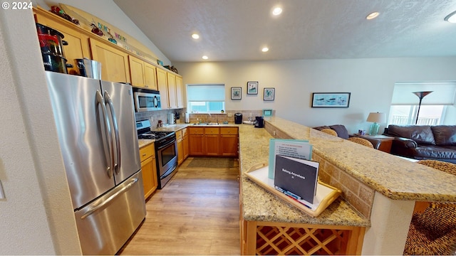 kitchen with sink, light hardwood / wood-style flooring, backsplash, kitchen peninsula, and appliances with stainless steel finishes