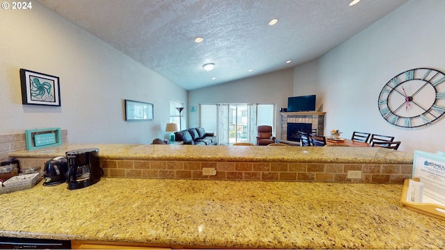 kitchen featuring dishwasher, light stone counters, a textured ceiling, vaulted ceiling, and a fireplace