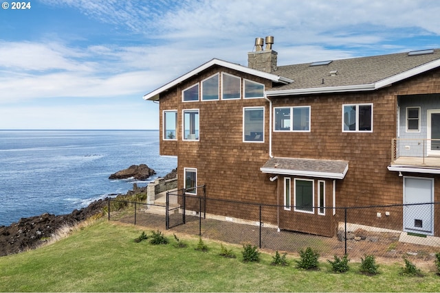 rear view of house featuring a water view and a lawn