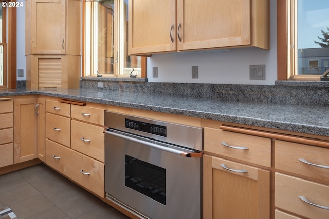 kitchen with stainless steel oven, dark tile patterned flooring, and light brown cabinetry