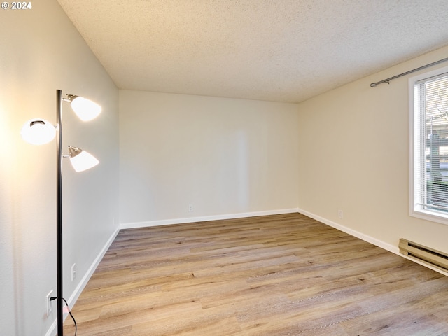 unfurnished room featuring a textured ceiling, baseboard heating, and light wood-type flooring