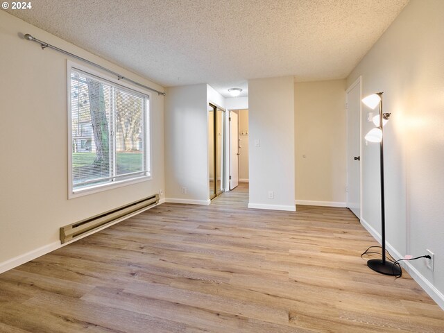 empty room featuring a baseboard heating unit, light hardwood / wood-style flooring, and a textured ceiling