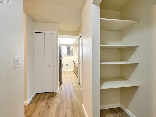 corridor with light hardwood / wood-style floors and a textured ceiling