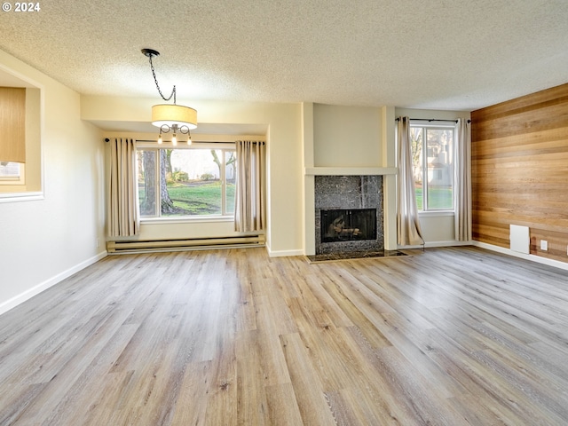 unfurnished living room with a tiled fireplace, light wood-type flooring, a wealth of natural light, and baseboard heating