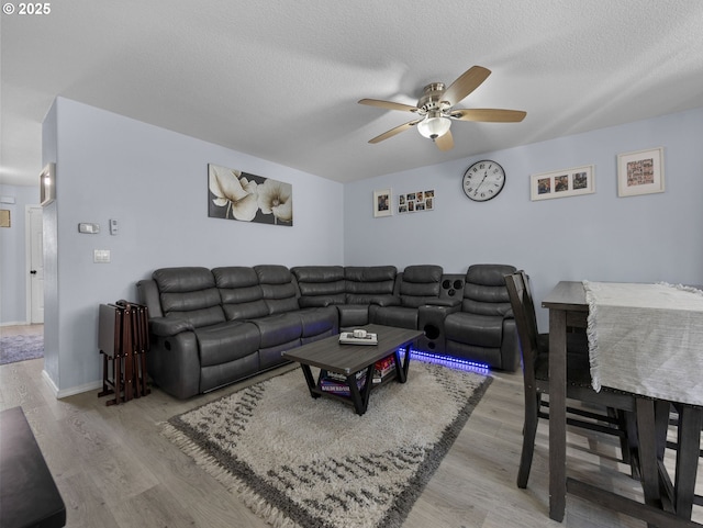 living area with baseboards, wood finished floors, a ceiling fan, and a textured ceiling