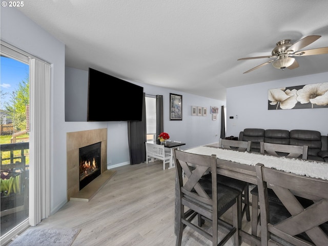 dining space featuring a textured ceiling, light wood-style flooring, ceiling fan, baseboards, and a tiled fireplace