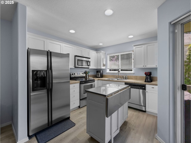 kitchen with white cabinets, a center island, appliances with stainless steel finishes, and a sink
