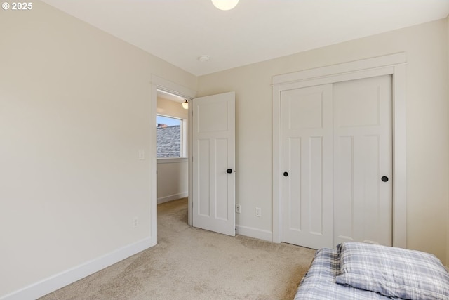 bedroom with a closet, light carpet, and baseboards