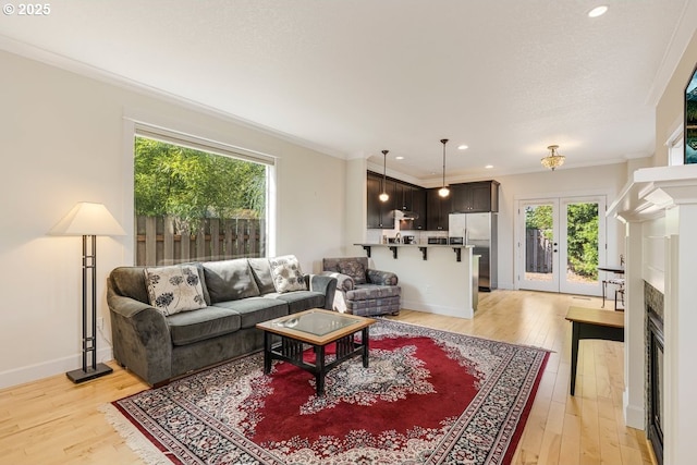 living room featuring light wood-style floors, a fireplace, crown molding, and french doors