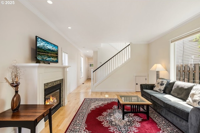 living room with light wood finished floors, stairs, a fireplace, and crown molding