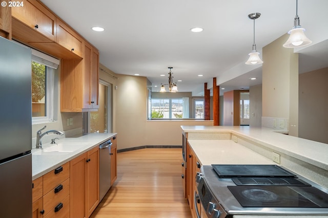549 N Tomahawk Island Dr # 1, Portland, OR 97217 - kitchen featuring stainless steel appliances, light countertops, a sink, light wood-type flooring, and hanging light fixtures