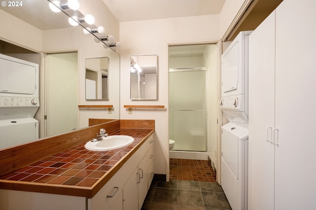 bathroom with toilet, a shower with shower door, stacked washer and clothes dryer, and vanity