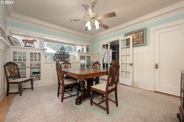 dining area featuring crown molding, a ceiling fan, light wood-style flooring, and a decorative wall