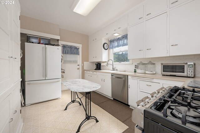 kitchen featuring dishwasher, light countertops, freestanding refrigerator, and white cabinets