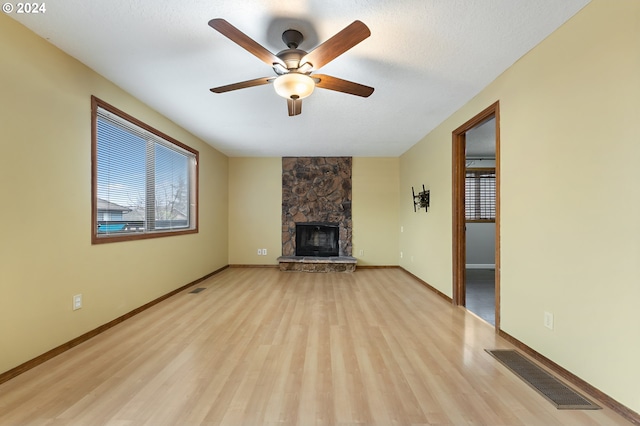 unfurnished living room featuring ceiling fan, a stone fireplace, a textured ceiling, and light hardwood / wood-style flooring