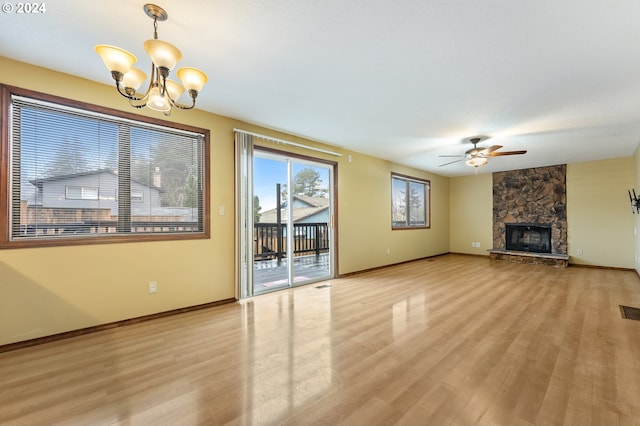 unfurnished living room featuring ceiling fan with notable chandelier, light hardwood / wood-style floors, and a stone fireplace