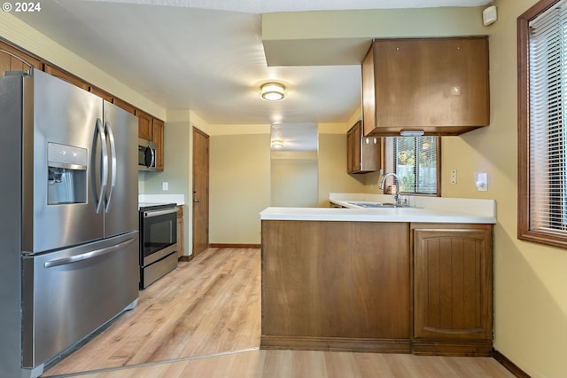 kitchen with kitchen peninsula, stainless steel appliances, light hardwood / wood-style floors, and sink