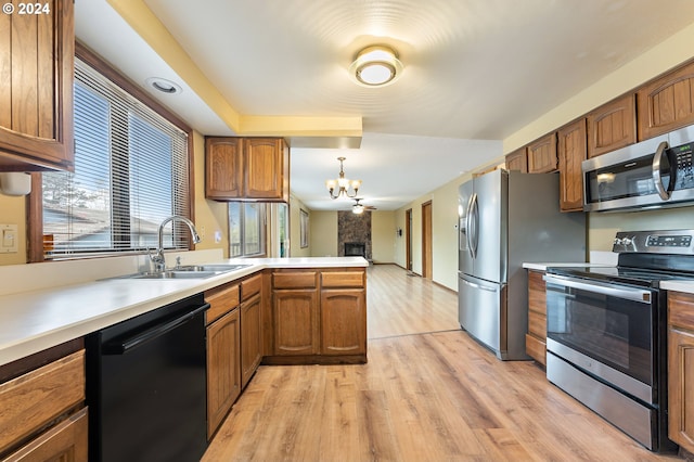 kitchen featuring pendant lighting, sink, light wood-type flooring, a fireplace, and appliances with stainless steel finishes