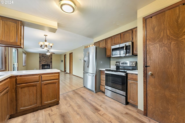 kitchen featuring appliances with stainless steel finishes, ceiling fan with notable chandelier, decorative light fixtures, a fireplace, and light hardwood / wood-style floors