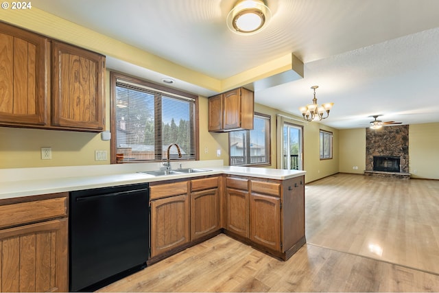 kitchen featuring kitchen peninsula, sink, dishwasher, a stone fireplace, and hanging light fixtures