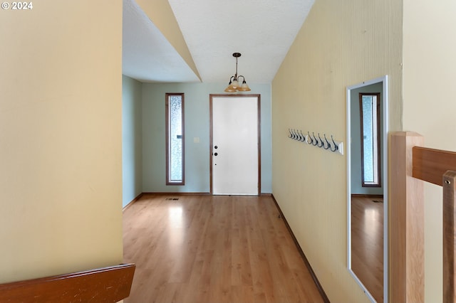 entryway with light hardwood / wood-style flooring, a textured ceiling, and an inviting chandelier