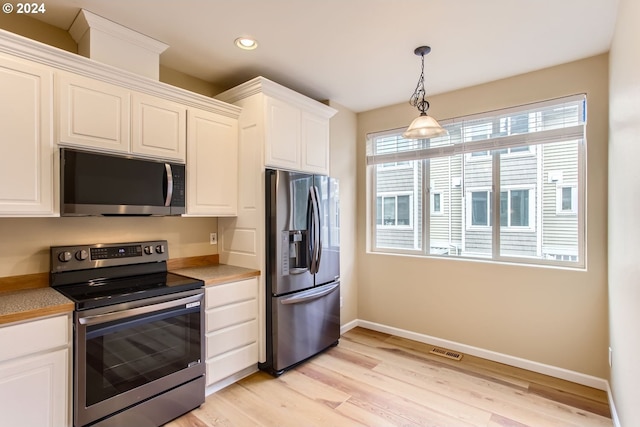 kitchen featuring white cabinets, appliances with stainless steel finishes, light hardwood / wood-style flooring, and hanging light fixtures