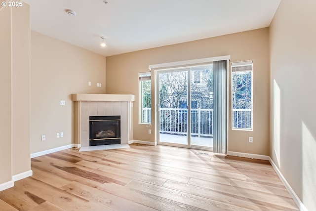 unfurnished living room with a tiled fireplace and light hardwood / wood-style flooring