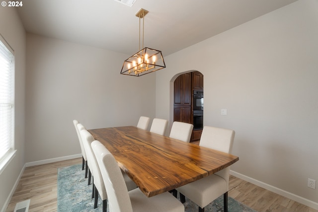 dining space with arched walkways, visible vents, a notable chandelier, and light wood-style flooring