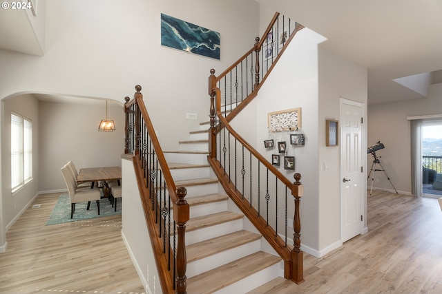 staircase with arched walkways, wood finished floors, a towering ceiling, and baseboards