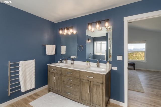 full bath with double vanity, a sink, baseboards, and wood finished floors