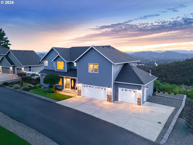 view of front facade with a garage, driveway, stone siding, roof with shingles, and a mountain view