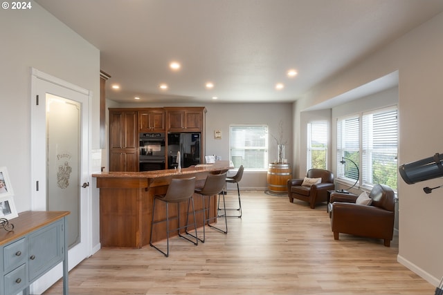 kitchen with a breakfast bar area, light wood finished floors, open floor plan, a peninsula, and black appliances