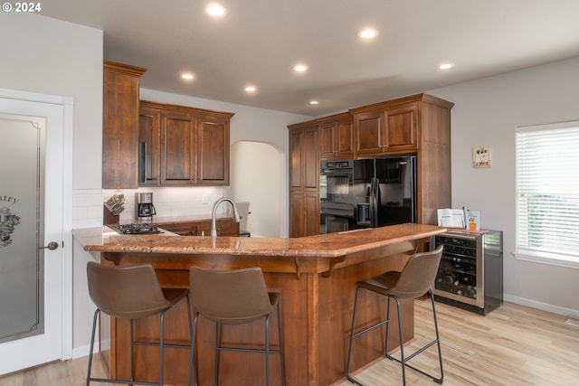 kitchen featuring light stone counters, a sink, black appliances, a peninsula, and a kitchen breakfast bar