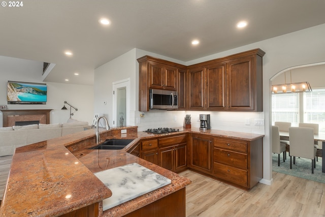 kitchen featuring light wood finished floors, stainless steel microwave, decorative backsplash, a sink, and black gas stovetop