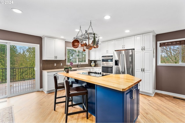 kitchen featuring a healthy amount of sunlight, white cabinetry, stainless steel appliances, and wooden counters