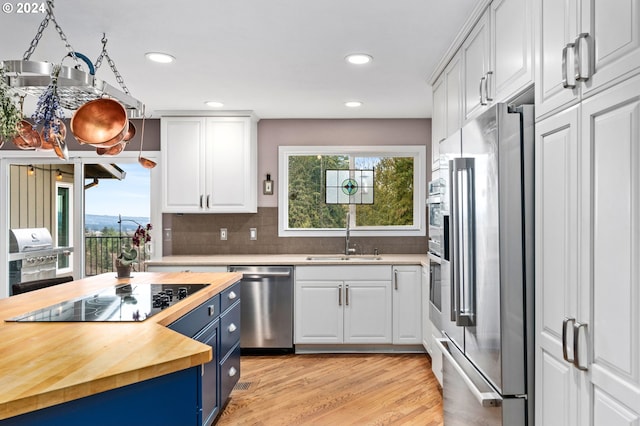 kitchen with blue cabinetry, butcher block counters, white cabinets, and stainless steel appliances