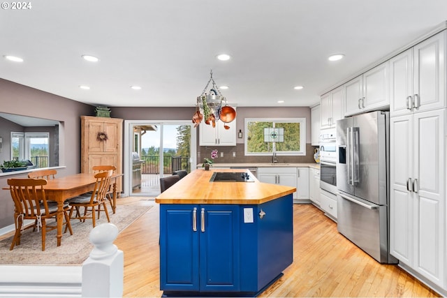 kitchen with appliances with stainless steel finishes, light wood-type flooring, white cabinetry, and a healthy amount of sunlight