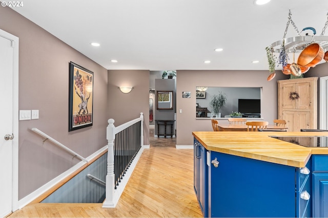 kitchen with black electric stovetop, light hardwood / wood-style floors, blue cabinets, and butcher block counters