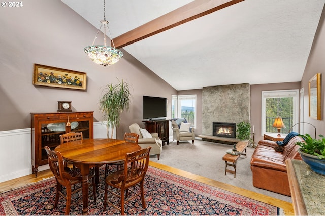 dining room featuring lofted ceiling with beams, a healthy amount of sunlight, wood-type flooring, and a fireplace