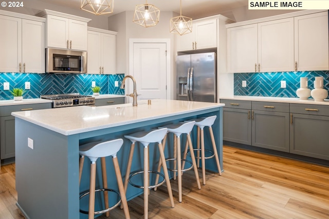 kitchen with gray cabinetry, stainless steel appliances, a center island with sink, pendant lighting, and light hardwood / wood-style floors