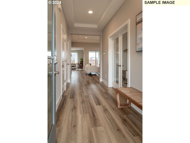 corridor with french doors, a raised ceiling, and wood-type flooring